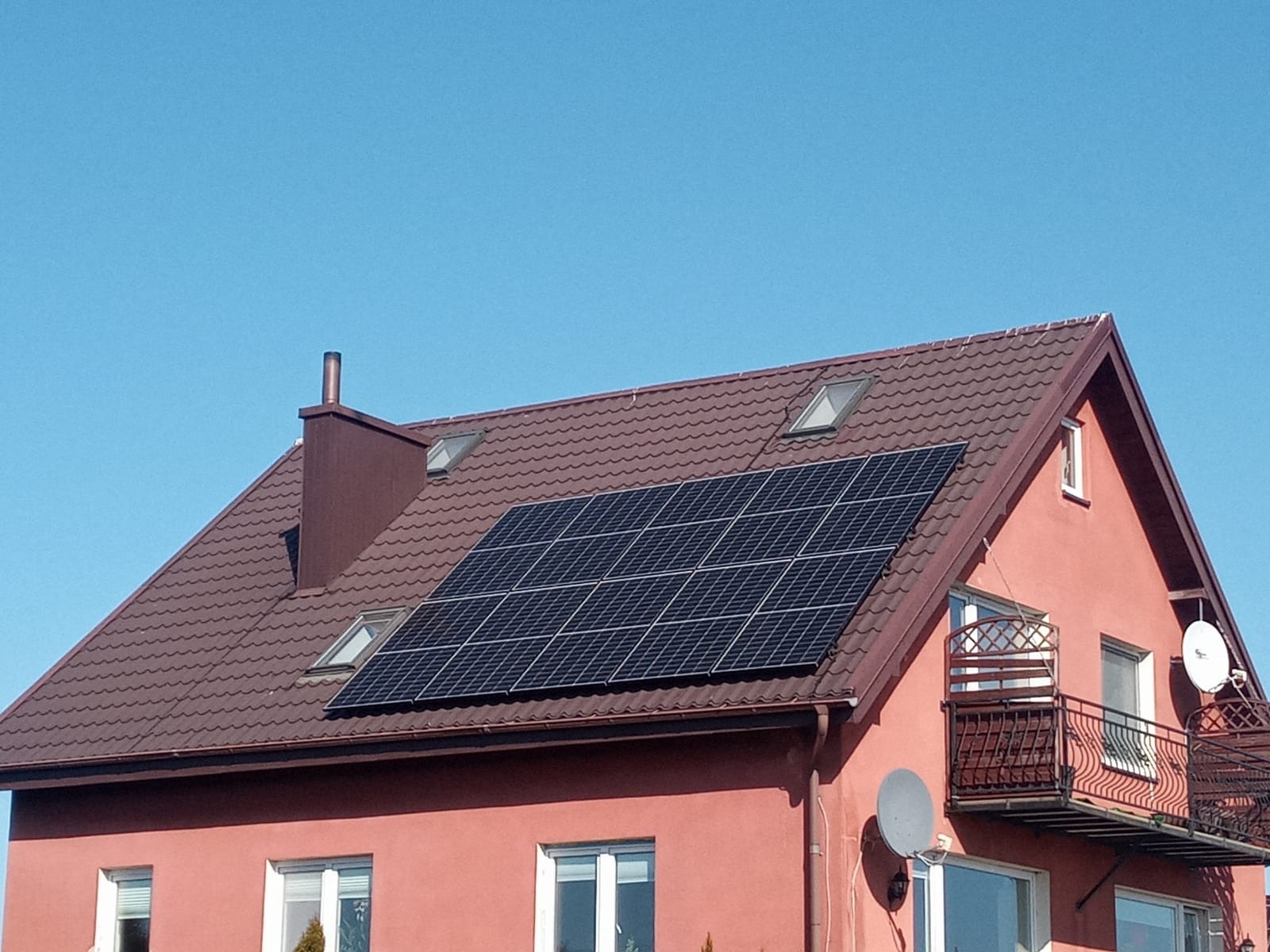 Panele słoneczne na dachu domu w Chojnicach, widoczne okna dachowe i komin.