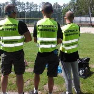 Trzech mężczyzn w odblaskowych kamizelkach z napisem 'czyściochy.pl firma sprzątająca' stoi tyłem na tle parku z workami na śmieci.