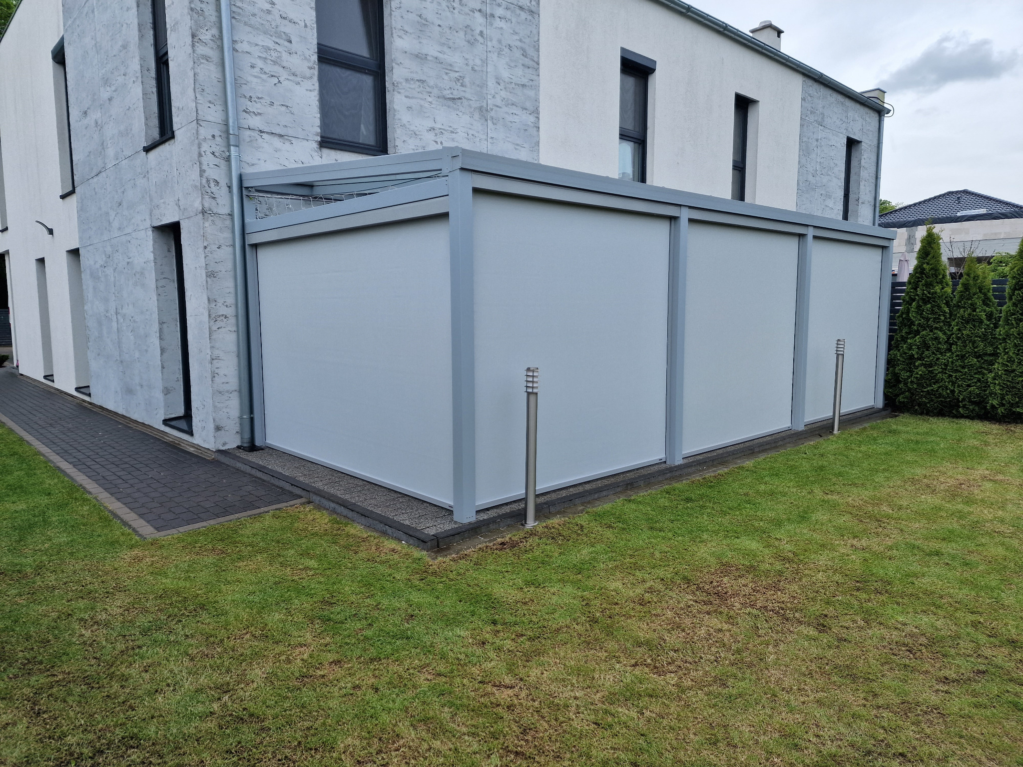 Zewnętrzna konstrukcja osłonowa z szarego materiału przy nowoczesnym domu z szarym trawnikiem.