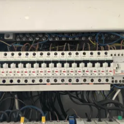 Rozdzielnica elektryczna z widocznymi bezpiecznikami różnicowoprądowymi i nadprądowymi marki Moeller oraz przewodami wewnątrz skrzynki, z bliska.