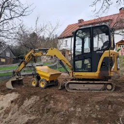 Żółta mini koparka CAT i wywrotka na placu budowy, dom w tle. Widoczne ślady pracy w ziemi. Sprzęt Zeppelin.