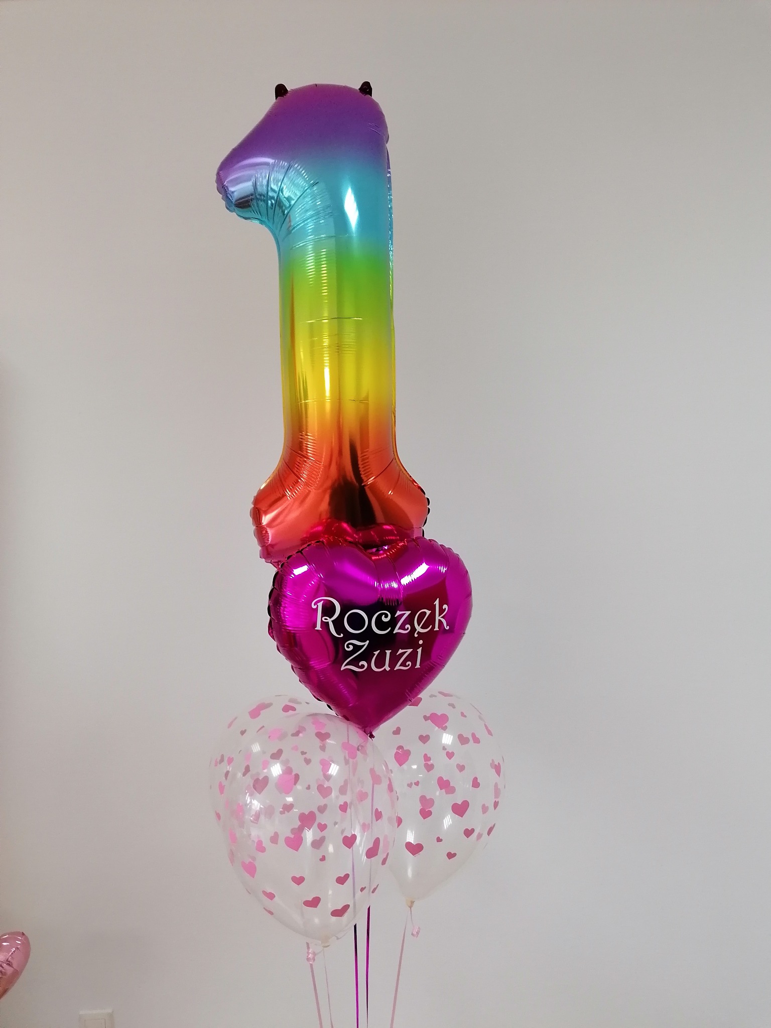 Balonowy bukiet na roczek Zuzi: tęczowa cyfra '1', różowe serce z napisem i przezroczyste balony w różowe serduszka.