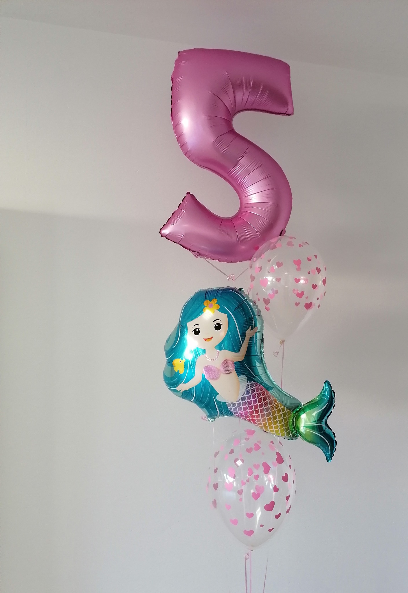 Zestaw balonów: duża, różowa cyfra 5, balon w kształcie syrenki z turkusowymi włosami i dwa przezroczyste balony z drobnymi, różowymi serduszkami, na białym tle.