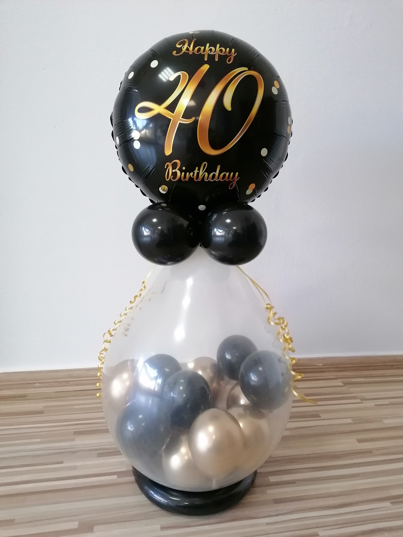 Dekoracja balonowa na 40 urodziny: czarny balon foliowy z napisem 'Happy 40 Birthday' nad transparentnym balonem wypełnionym złotymi i szarymi balonami.