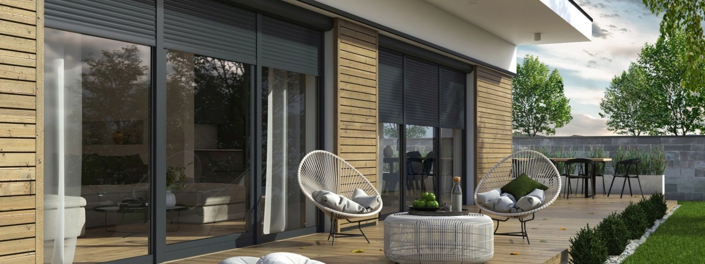 Zewnętrzny taras z drewnianą podłogą, meblami ogrodowymi i dużymi oknami zabezpieczonymi roletami w kolorze antracytowym.
