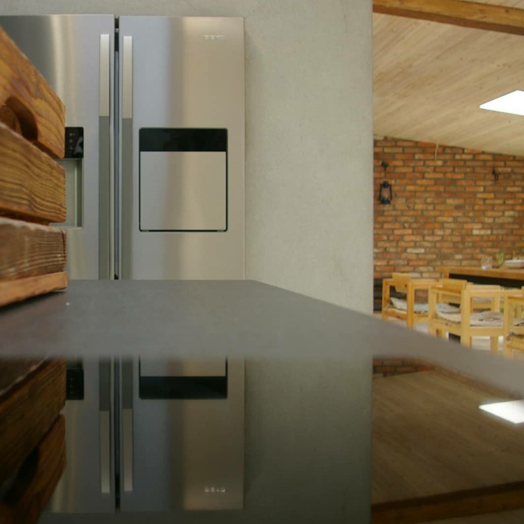 Nowoczesna kuchnia z metalową lodówką side-by-side, drewnianymi akcentami i widokiem na ceglaną ścianę jadalni w tle.