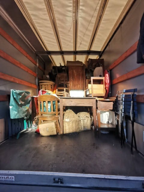 Wnętrze samochodu dostawczego wypełnione meblami i przedmiotami, w tym krzesłami, stołem, szafą i wiklinowymi koszami, zabezpieczonymi na czas transportu.