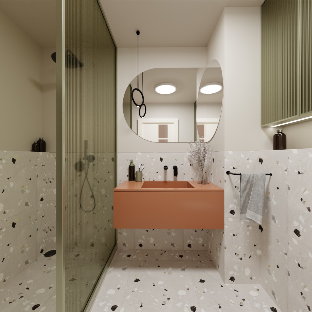 Nowoczesna łazienka z kabiną prysznicową oddzieloną szkłem ryflowanym, umywalką w kolorze terakoty i lustrem o zaokrąglonym kształcie. Na ścianach i podłodze płytki imitujące lastryko.
