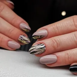 Dłonie z beżowymi i czarnymi paznokciami z abstrakcyjnym wzorem w paski w kolorze złota i czerni, na jasnym tle.