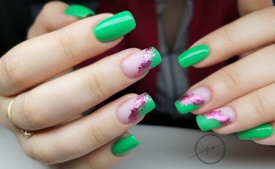 Dłonie z zielonymi paznokciami, niektóre z brokatową, różową folią na końcówkach, pierścionek na palcu wskazującym.