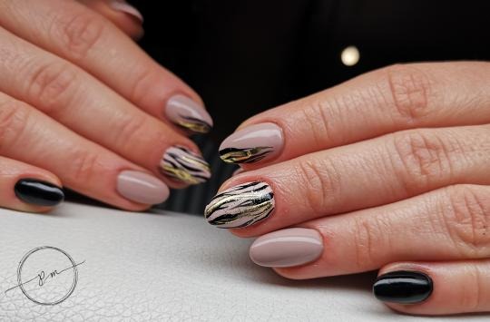 Dłonie z beżowymi i czarnymi paznokciami z abstrakcyjnym wzorem w paski w kolorze złota i czerni, na jasnym tle.