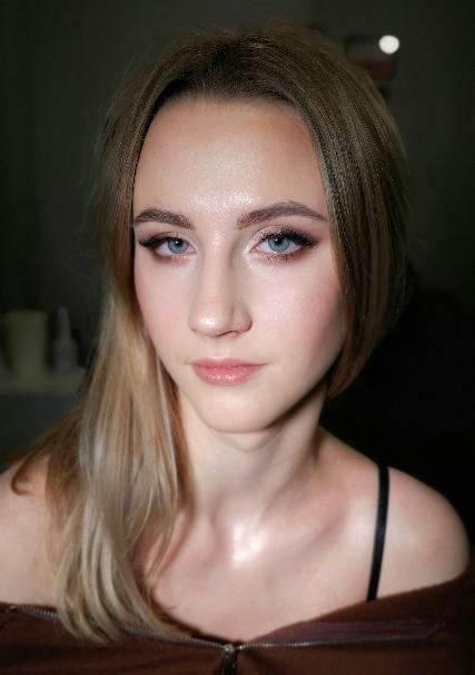 Portret młodej kobiety z delikatnym, dziennym makijażem: subtelnie podkreślone oczy z czarną kreską, rozświetlony wewnętrzny kącik oka, róż na policzkach i błyszczyk na ustach.