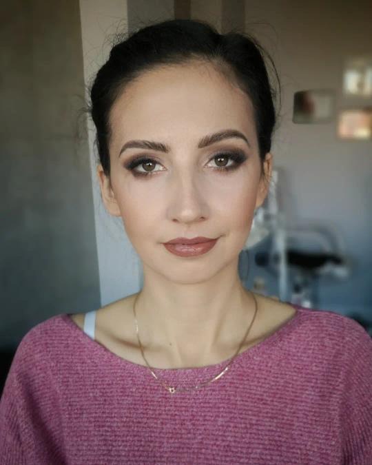 Portret kobiety z profesjonalnym makijażem oczu w odcieniach brązu i ustami w kolorze nude, delikatna biżuteria na szyi, sweter w kolorze fuksji.