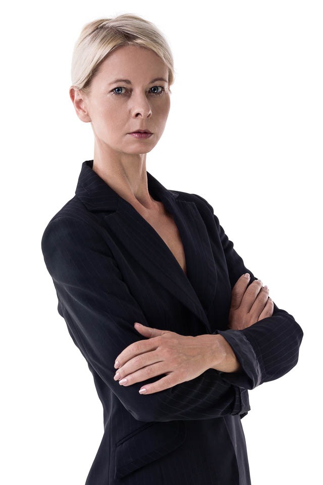 Portret kobiety w ciemnym garniturze w paski, z założonymi rękami na białym tle.