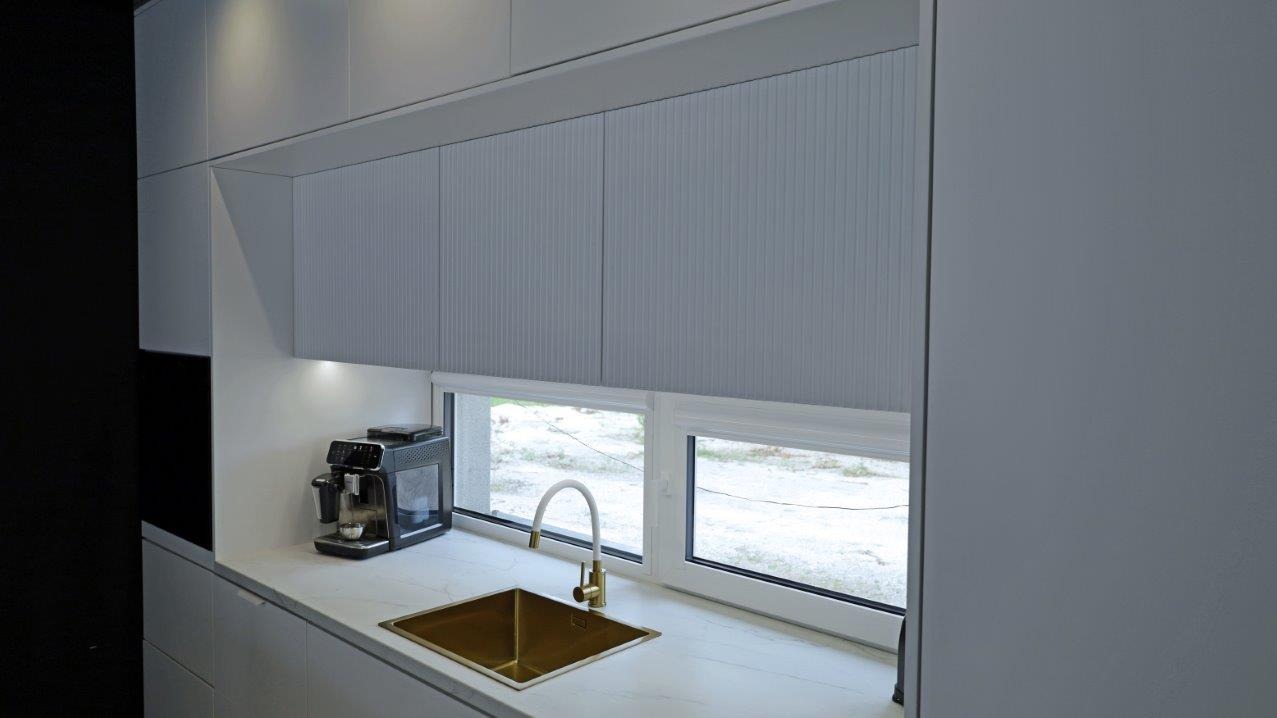 Nowoczesna kuchnia z szarymi szafkami z ryflowanymi frontami, złotym zlewem i ekspres do kawy na blacie z białego marmuru.