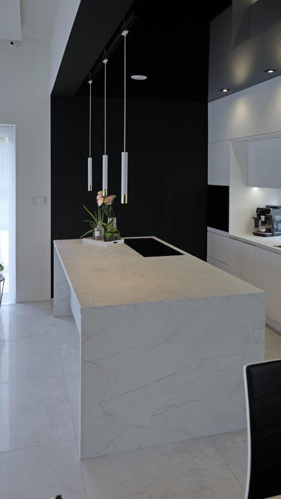 Wyspa kuchenna z marmurowym blatem i płytą indukcyjną, minimalistyczne lampy wiszące. Nowoczesna kuchnia we Wrocławiu w bieli i czerni.