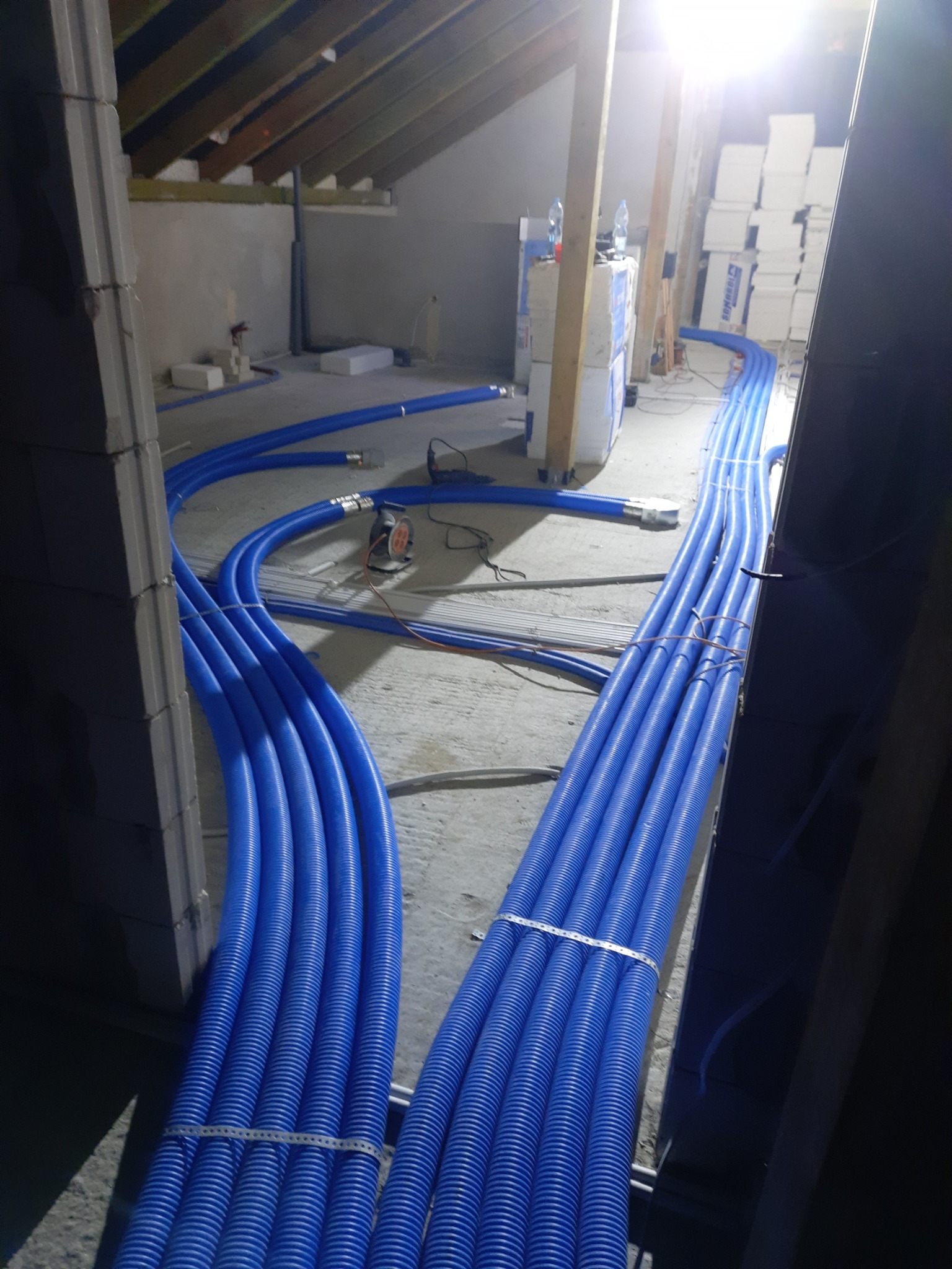 Niebieskie rury wentylacyjne prowadzone pod skosem poddasza w Juchnowcu Kościelnym, widoczne narzędzia i materiały budowlane.