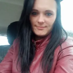 Portret kobiety z długimi, ciemnymi włosami w czerwonej skórzanej kurtce, zrobiony w samochodzie, z widocznym fragmentem tylnego siedzenia.