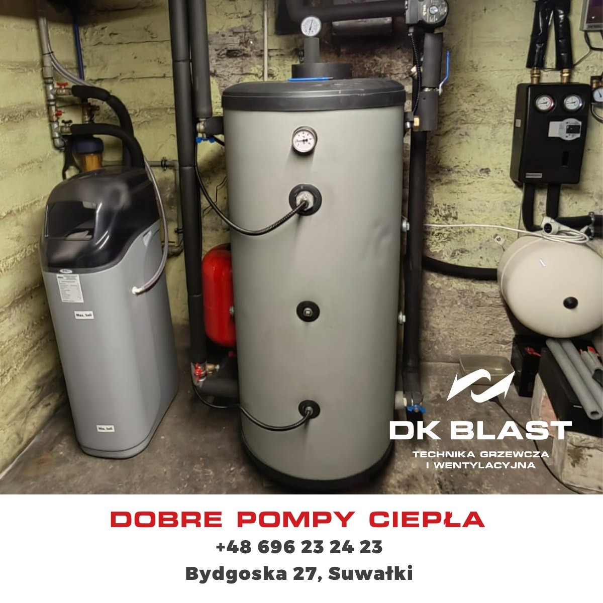 Szara, pionowa instalacja z manometrami i przyłączami, obok zmiękczacz wody w szarej obudowie, na tle surowej ściany w piwnicy.