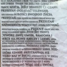 Kartka z motywacyjnym tekstem 'To jest Twoje życie...' w czcionce maszynowej, leżąca na pogniecionej powierzchni, z czerwonym pąkiem róży w prawym górnym rogu.