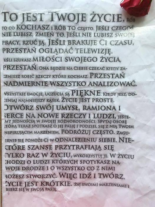 Kartka z motywacyjnym tekstem 'To jest Twoje życie...' w czcionce maszynowej, leżąca na pogniecionej powierzchni, z czerwonym pąkiem róży w prawym górnym rogu.