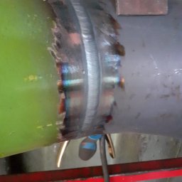 Instal-Spaw - Spoina na rurze łączącej elementy instalacji, widoczne ślady obróbki termicznej i przebarwienia metalu. Zastosowano uchwyt stabilizujący podczas spawania.