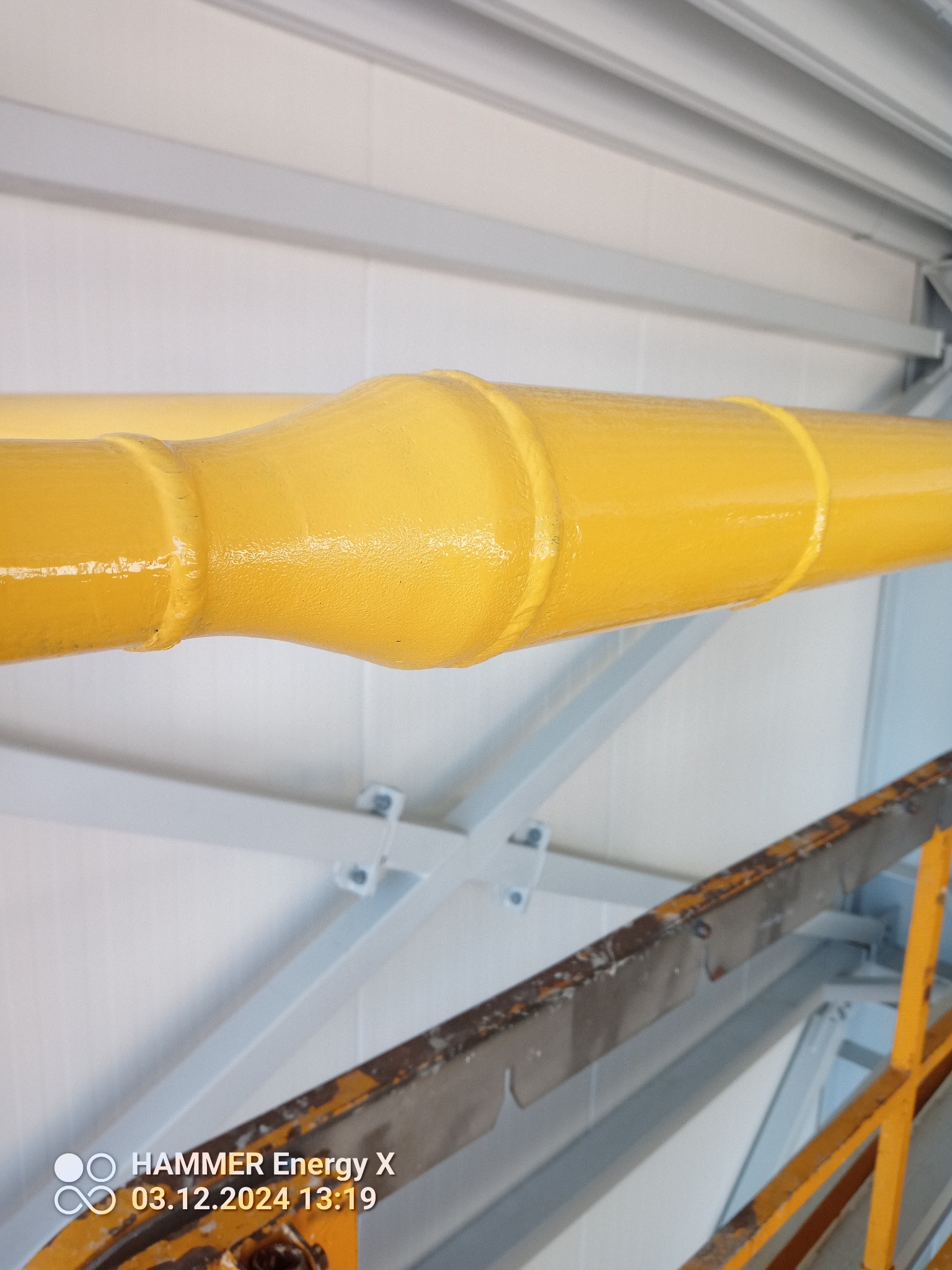 Żółty spaw na rurze gazowej wewnątrz budynku, widoczny z bliska, z elementami rusztowania w tle. Spaw wykonany z dbałością o szczegóły.