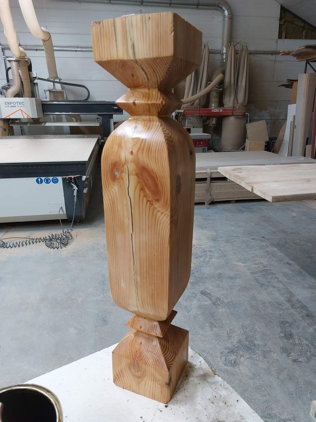 Toczone drewniane tralki schodowe z widocznym pęknięciem, w tle maszyna CNC w warsztacie stolarskim.