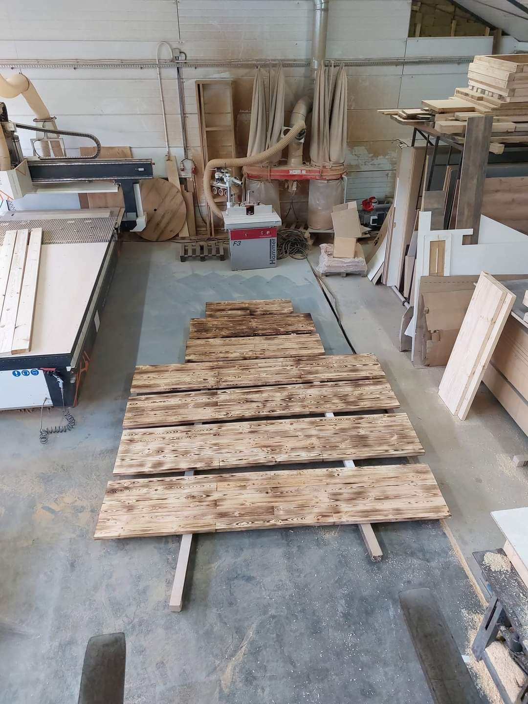 Warsztat stolarski: deski z wypalanym wzorem leżące na podkładkach, w tle maszyny do obróbki drewna i materiały