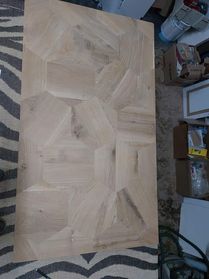 Blat drewniany z geometrycznym wzorem, jasne drewno, widoczne słoje, w tle kartony i narzędzia.