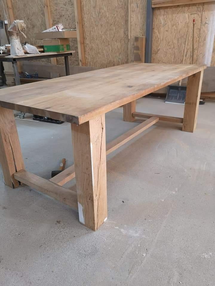 Surowy, drewniany stół z grubych belek w warsztacie, widoczne niedoskonałości i ślady obróbki, w tle deski i narzędzia.