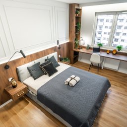Marta Rudnicka (Rudnicka Interiors) - Jasna sypialnia z drewnianą zabudową, biurkiem przy oknie i szarą narzutą na łóżku, widok z góry.