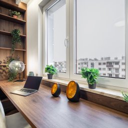 Marta Rudnicka (Rudnicka Interiors) - Nowoczesne biuro domowe z drewnianym biurkiem, laptopem, lampą kulą i roślinami doniczkowymi przy oknie z widokiem na miasto.