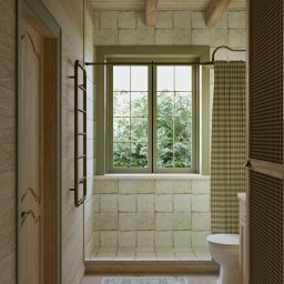 Marta Rudnicka (Rudnicka Interiors) - Rustykalna łazienka z drewnianymi panelami, zielonym oknem z widokiem na bujną zieleń, beżowymi płytkami, kratkowaną zasłoną prysznicową i drewnianymi belkami sufitowymi.