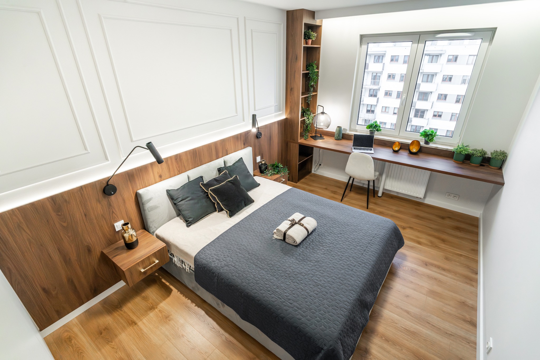 Jasna sypialnia z drewnianą zabudową, biurkiem przy oknie i szarą narzutą na łóżku, widok z góry.