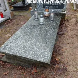 Granitowy pomnik z napisem 'AVE MARIA' i czterema lampionami, otoczony ziemią i opadłymi liśćmi na cmentarzu.