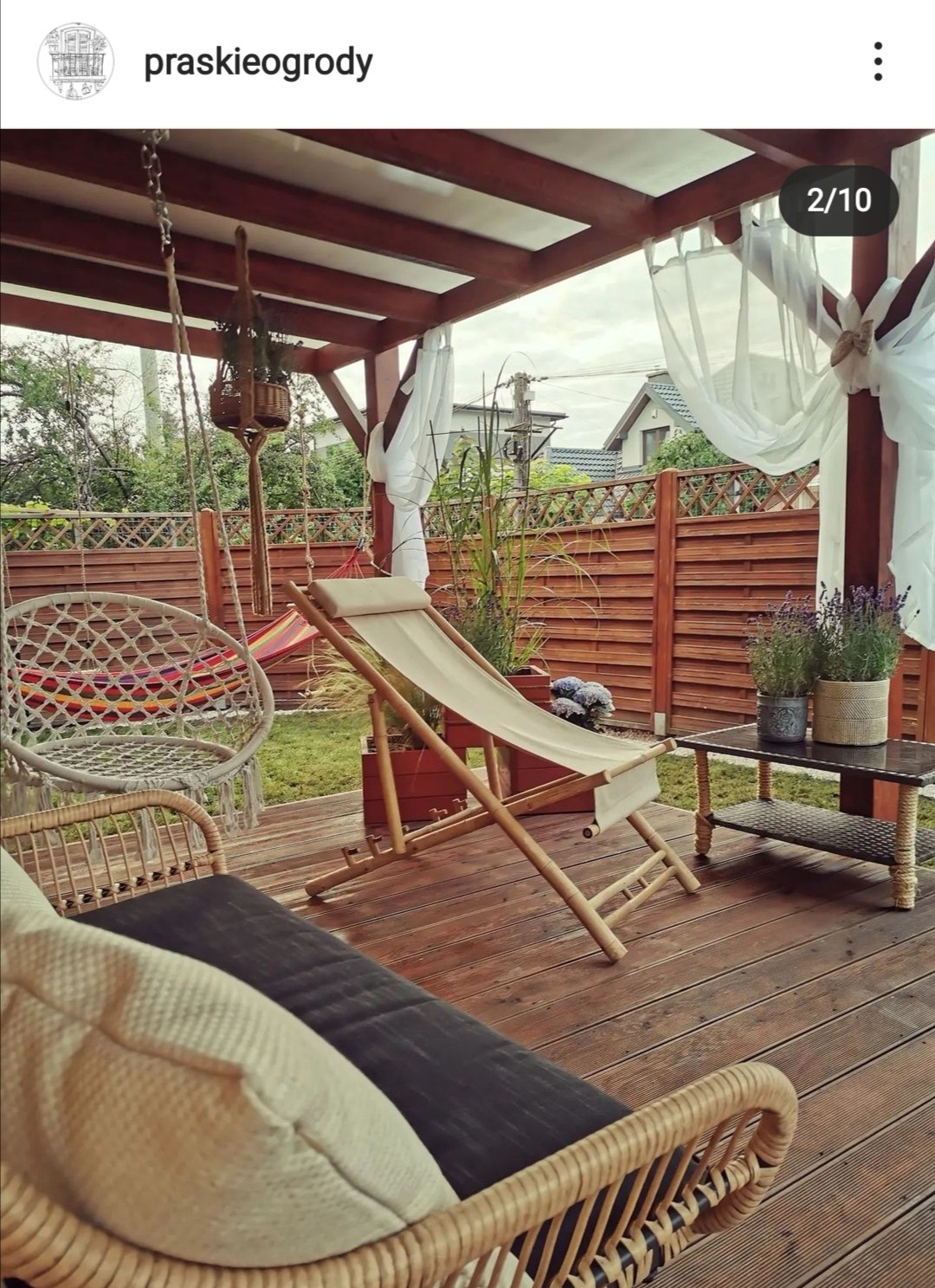 Zadaszony taras z drewnianą podłogą, wyposażony w rattanowy fotel, hamak w stylu boho, leżak oraz stolik z lawendą w doniczkach, udekorowany białymi, zwiewnymi zasłonami.