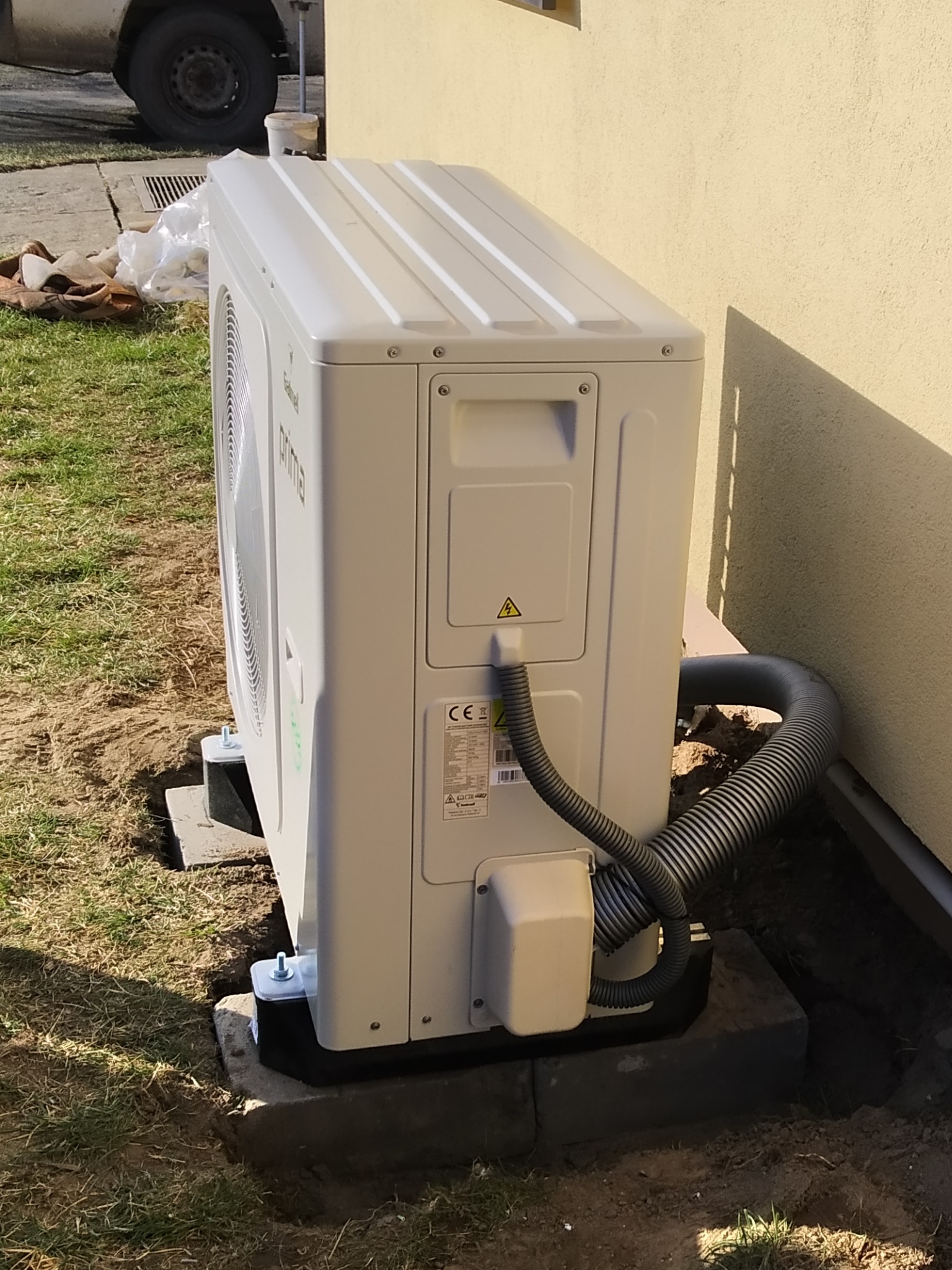 Zewnętrzna jednostka klimatyzacji marki Galmet Prima zamontowana na betonowych podstawach przy ścianie budynku, widoczny przewód odprowadzający skropliny.