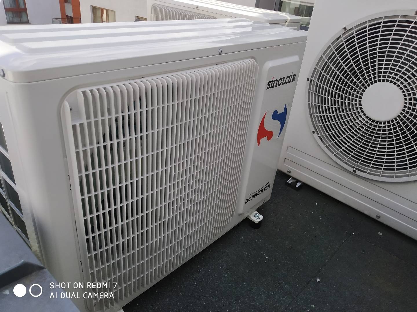 Dwa białe, zewnętrzne agregaty klimatyzacyjne marki Sinclair z widocznym logo i oznaczeniem DC Inverter, ustawione na płaskim, ciemnym dachu budynku.