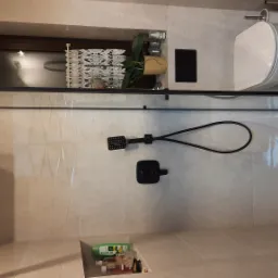 Nowoczesna kabina prysznicowa typu walk-in z czarną armaturą, widok z góry ukazuje odpływ liniowy, białą ceramikę sanitarną i półki wnękowe z kosmetykami oraz rośliną doniczkową.