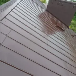 Ciemnobrązowy, metalowy dach panelowy z kominem w tle, widok z góry, lekki połysk na powierzchni.