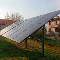 Panel słoneczny na metalowej konstrukcji ustawiony na trawniku przed domem jednorodzinnym w słoneczny dzień.