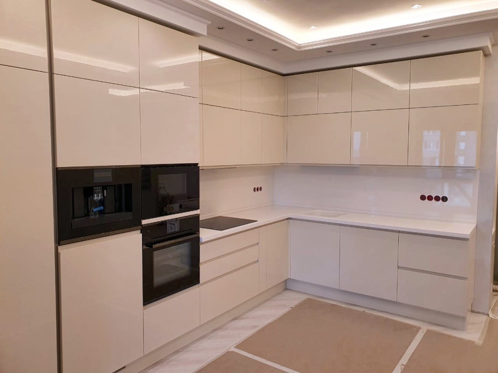 Jasna, nowoczesna kuchnia w Warszawie z zabudową meblową pod sufit, wbudowanym ekspresem do kawy i piekarnikiem, oraz minimalistycznym oświetleniem sufitowym.