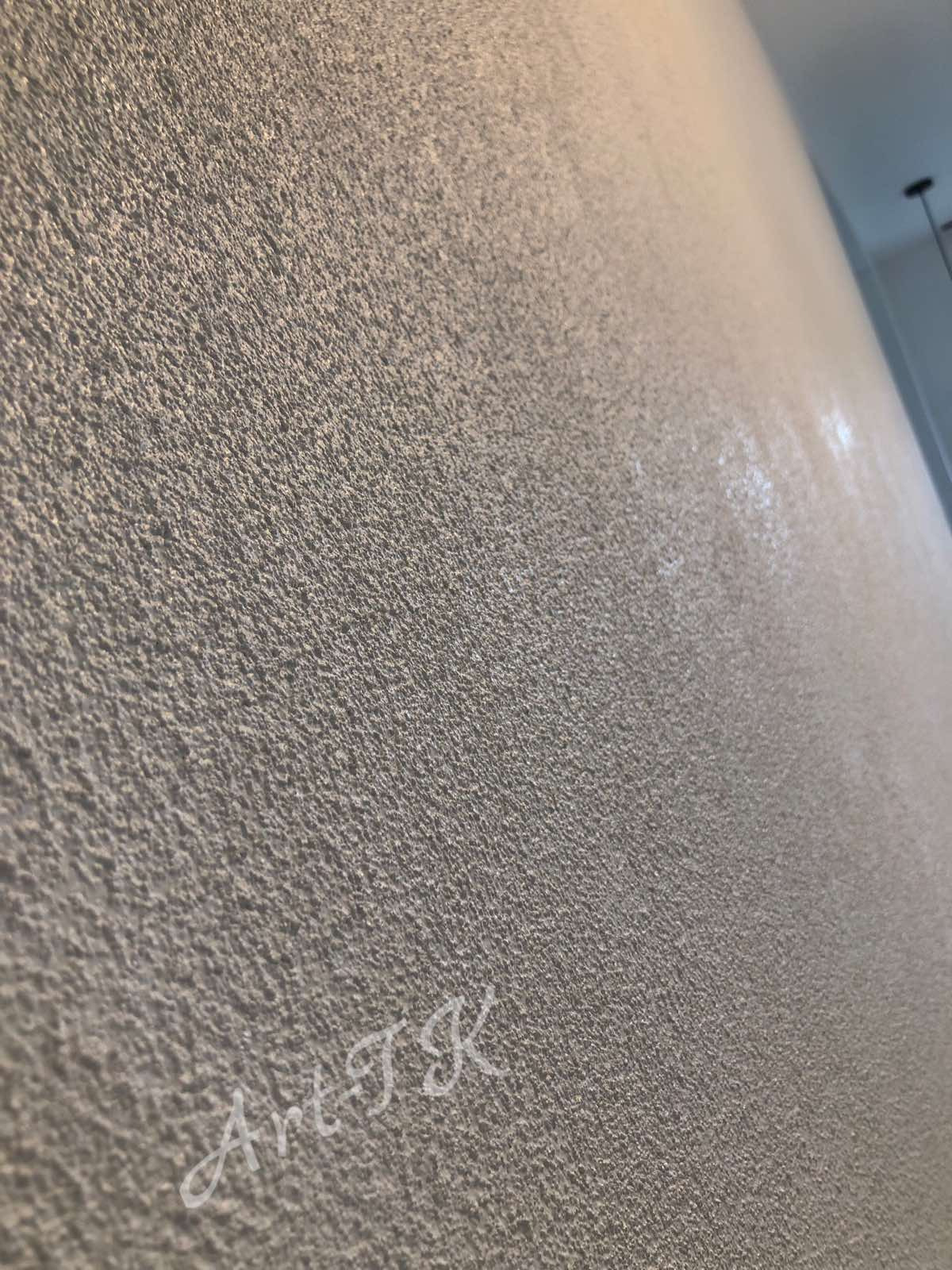 Szara ściana z wyraźną, ziarnistą fakturą, oświetlona z góry, z widocznym odblaskiem światła i delikatnym, odręcznym napisem 'ArtTK' w lewym dolnym rogu.