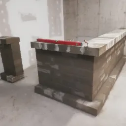 Wznoszenie murowanej ścianki działowej z cegieł w surowym wnętrzu, widoczny poziomica i kielnia, ściany w stanie deweloperskim.