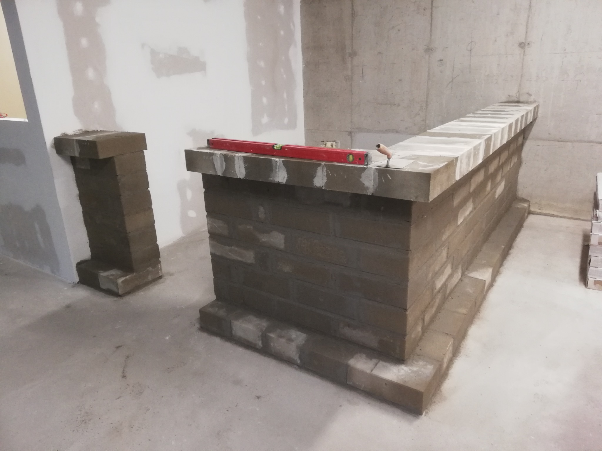 Wznoszenie murowanej ścianki działowej z cegieł w surowym wnętrzu, widoczny poziomica i kielnia, ściany w stanie deweloperskim.