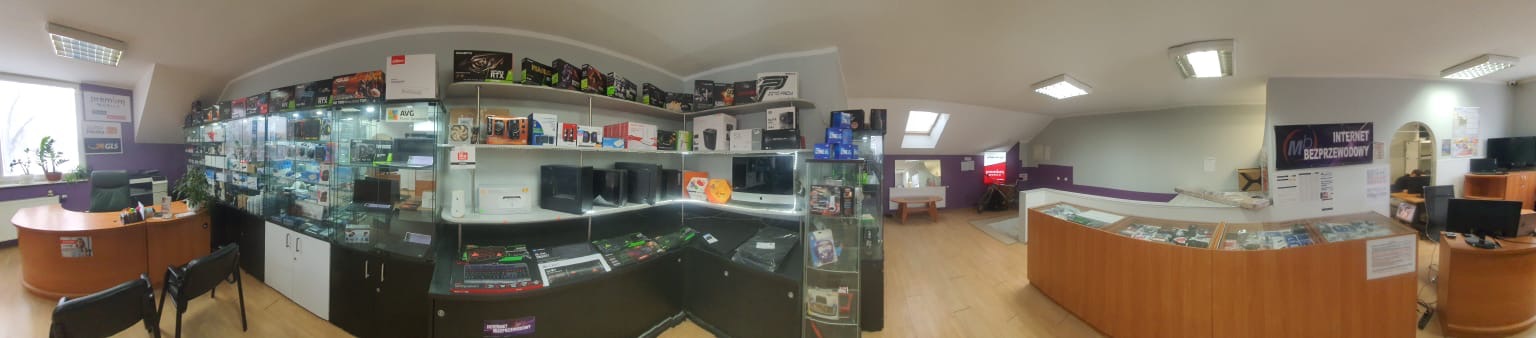 Wnętrze sklepu komputerowego z ekspozycją sprzętu, biurkiem obsługi klienta i plakatem reklamującym bezprzewodowy dostęp do sieci.