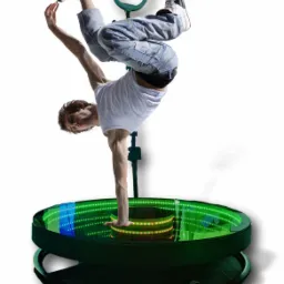 Mężczyzna wykonuje akrobatyczny taniec na obrotowej platformie z podświetleniem LED, ubrany w białą koszulkę i dżinsy.