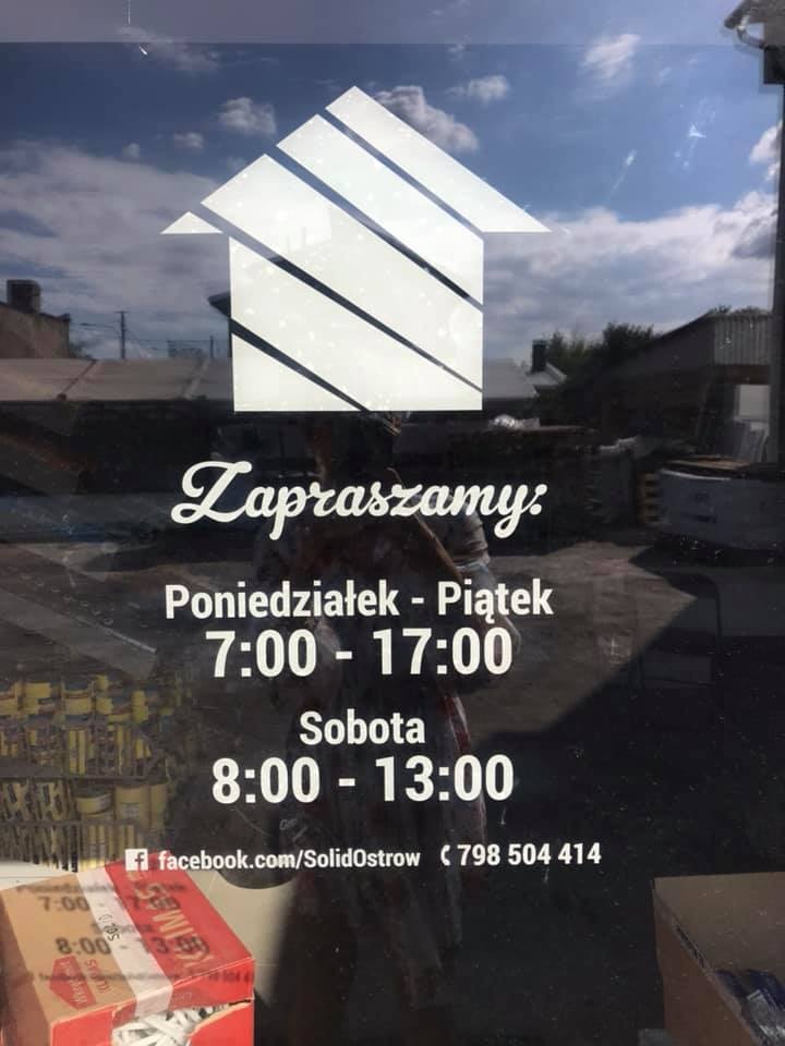 Witraż na szybie z logo domu i napisem 'Zapraszamy', informujący o godzinach otwarcia od poniedziałku do piątku 7:00-17:00 i w sobotę 8:00-13:00, wraz z adresem profilu na Facebooku i numerem...