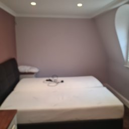 DB Remonty - Pokój z podwójnym łóżkiem i oknem w kształcie łuku, ściany pomalowane na dwa odcienie fioletu, widoczne ślady malowania przy suficie.